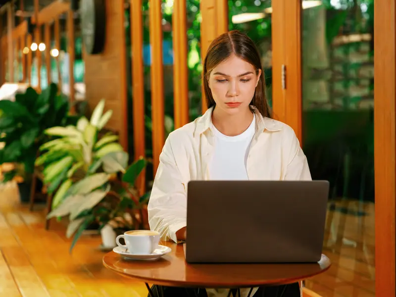 Une femme travaille sur un ordinateur portable à une table de café entourée de plantes