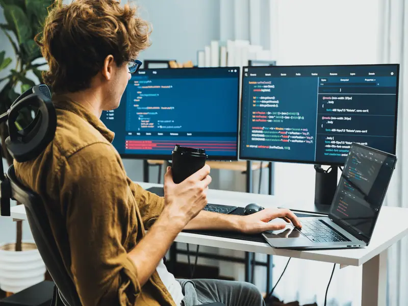Un développeur, une tasse à la main, devant deux écrans remplis de code